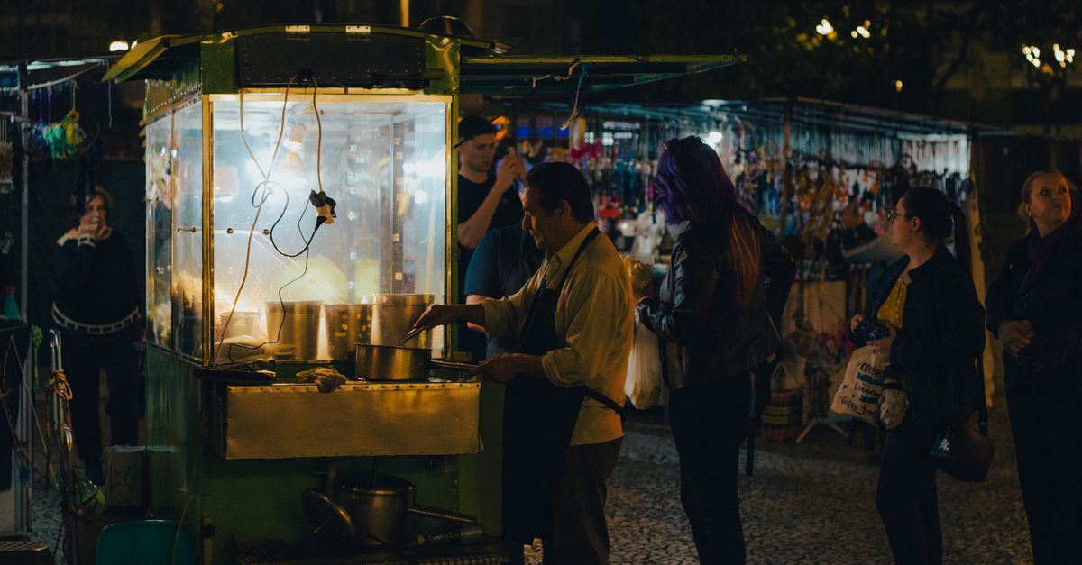 Puesto de comida callejera con un vendedor cocinando y clientes esperando cerca