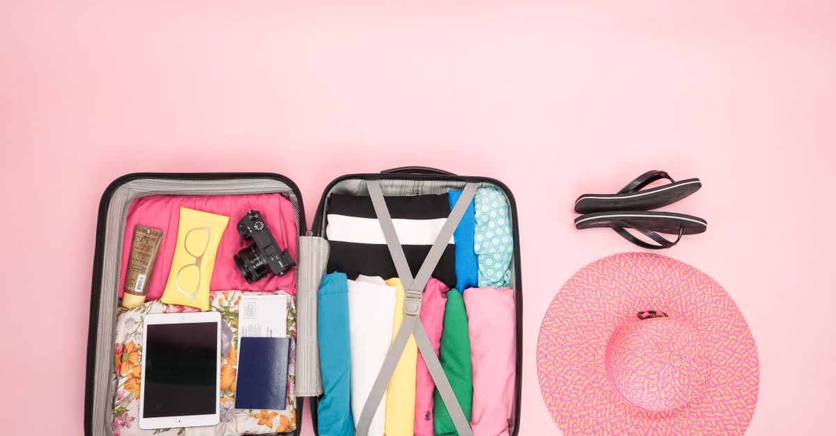 Maleta abierta sobre una cama con ropa doblada y artículos de viaje colocados cerca