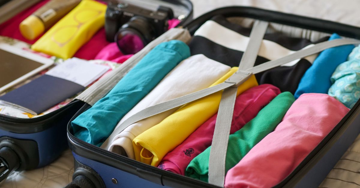 Open suitcase on a bed with folded clothes and travel items arranged nearby