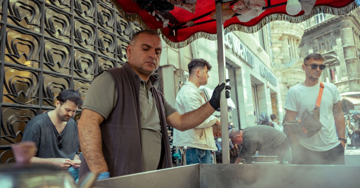 Puesto de comida callejera con un vendedor cocinando y clientes esperando cerca